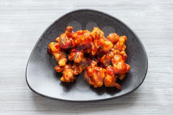 Korean Chinese cuisine - top view of Kkanpunggi spicy fried Chicken pieces with vegetables in sweet and sour sauce on black plate on gray table