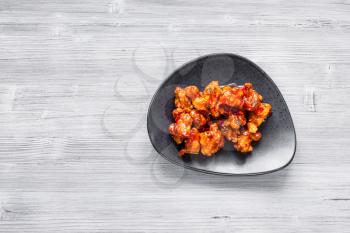 Korean Chinese cuisine - top view of Kkanpunggi spicy fried Chicken pieces with vegetables in sweet and sour sauce on black plate on gray table with copyspace