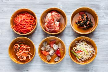 korean cuisine - top view of various side dishes (Banchan or Panchan) in ceramic bowls on gray table
