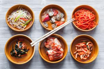 korean cuisine - chopsticks on bowls with various side dishes (Banchan or Panchan) on gray table