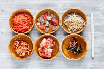 korean cuisine - top view of various side dishes (Banchan or Panchan) in ceramic bowls with chopsticks on gray table
