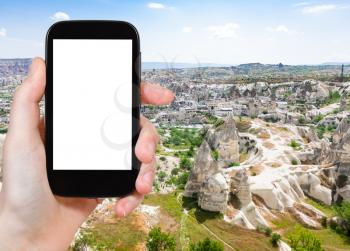 travel concept - tourist photographs of carved houses and Goreme town from mountain in Cappadocia in spring in Turkey on smartphone with empty cutout screen with blank place for advertising