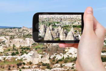 travel concept - tourist photographs of mountain valley with fairy chimney rocks in Goreme National Park in Cappadocia on smartphone in Turkey in spring