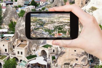 travel concept - tourist photographs of urban houses in rock-cut caves in Goreme town in Cappadocia on smartphone in Turkey in spring