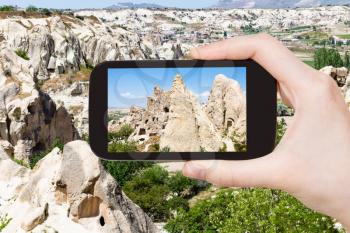 travel concept - tourist photographs of ancient rock-cut monastic settlement near Goreme town in Cappadocia on smartphone in Turkey in spring