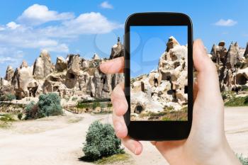 travel concept - tourist photographs of rock-cut ancient cave chapels near Goreme town in Cappadocia on smartphone in Turkey in spring