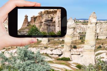 travel concept - tourist photographs of landscape with old fairy chimney rocks in mountains of Goreme National Park in Cappadocia on smartphone in Turkey in spring