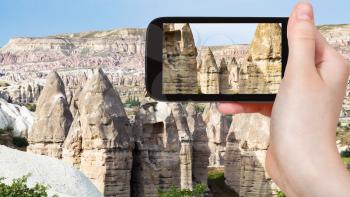 travel concept - tourist photographs of old fairy chimney rocks in mountain valley of Goreme National Park in Cappadocia on smartphone in Turkey in spring