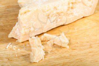 piece of local italian Parmigiano Reggiano (Parmesan) hard cheese with crumbs close up on light wooden cutting board
