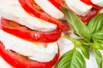 italian cuisine insalata caprese (caprese salad) - sliced mozzarella cheese and tomato with basil twig close up