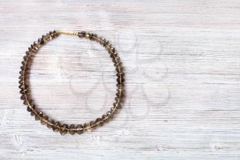 top view of faceted smoky quartz necklace on gray wooden board with copyspace