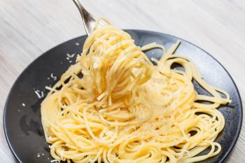 fork wrapped by spaghetti al burro e parmigiano (pasta with butter and cheese) over black plate on gray wooden table