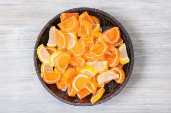 top view of sweet sugar lemon and orange marmalade slices in ceramic bowl on gray wooden board
