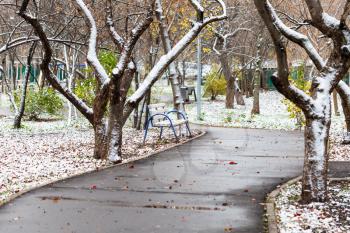 the first snow on bench and lawn and wet path in city park on autumn day