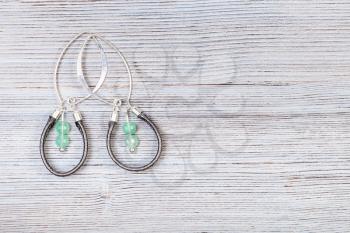 needlecraft background - handcrafted silver earrings from green jade and leather lace on gray wooden board with copyspace