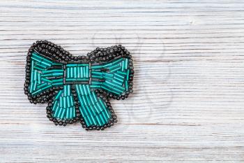 needlecraft background - top view of handcrafted bow tie brooch from glass green bugles and black beads on gray wooden board with copyspace