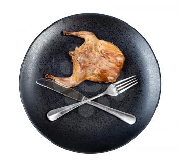 top view of roasted whole flattened quail with crossed fork and knife on black plate isolated on white background