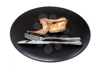 half of fried quail on black plate with fork and knife isolated on white background