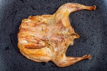 top view of roasted whole flattened quail on black plate