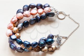 handmade bracelet from three stings of dyed natural river pearls and silver chain and clasp closeup on pale wooden table