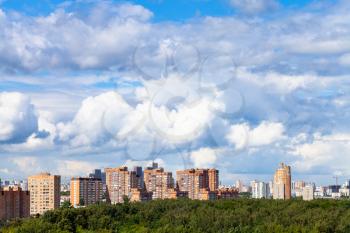 large white clouds in blue sky over apartment houses and green urban park in city on sunny summer day