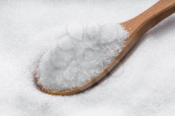 above view of wooden spoon with crystalline erythritol sugar substitute close up on pile of sugar
