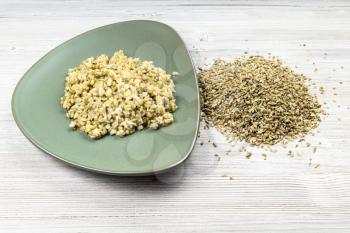 raw freekeh wheat grains and boiled porridge on green plate on wooden table
