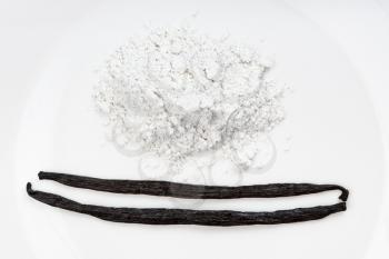 top view of whole vanilla beans and pile of vanilla sugar (sugar powder with ground natural vanilla) close up on white plate