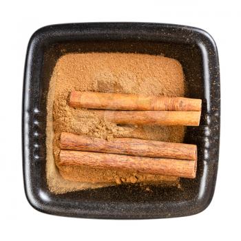 top view of cinnamon sticks and powder in black bowl isolated on white background