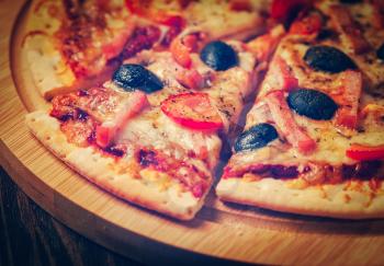 Vintage retro effect filtered hipster style image of sliced ham pizza with capsicum and olives on wooden board on table
