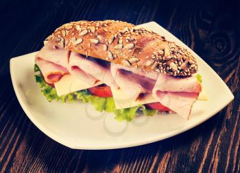 Vintage retro effect filtered hipster style image of ham sandwich with lettuce, cheese, tomato on plate on wooden table