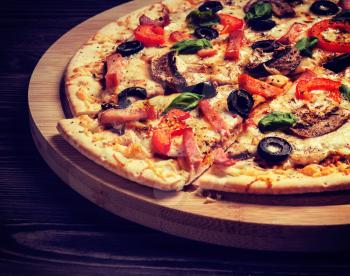 Vintage retro effect filtered hipster style image of ham pizza with capsicum, mushrooms, olives and basil leaves on wooden board on old table close up