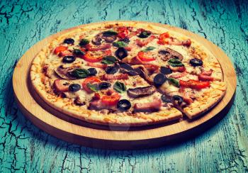 Vintage retro effect filtered hipster style image of ham pizza with capsicum, mushrooms, olives and basil leaves on wooden board on blue table