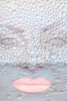 Pretty girl face with green eyes against transparent water drips as background.