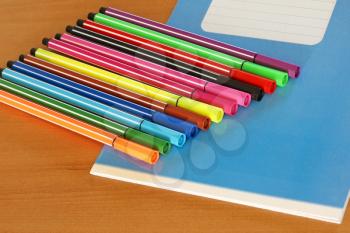 Blue writing book and multicolored pens on a wooden table.
