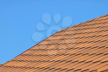 Roof of bituminous tiles against blue sky.
