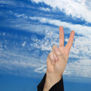 Man hand showing the victory sign on blue sky and white clouds background.