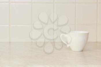 Ceramic tea cup on white kitchen table and ceramic tile background.