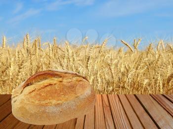 Warm crunchy bread on wooden surface against of ripe wheat ears and blue sky.