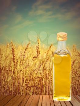 Vegetable oil on wooden surface against of wheat ears.Toned image.