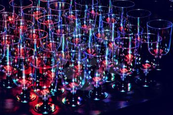 A row of wineglasses on holiday reception table in multicolored illumination.Toned image.