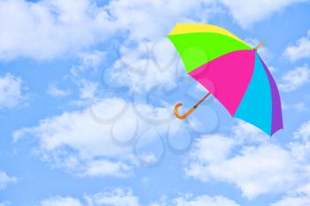 Multicolored umbrella flies in sky against of pure white clouds.Mary Poppins Umbrella.Wind of change concept.
