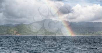 from a boat the rainbow from  ocean and island in background