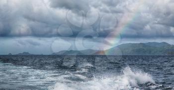 from a boat the rainbow from  ocean and island in background