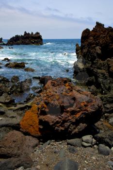 stone volcanic spain  water coast in lanzarote  sky cloud beach  and summer 
