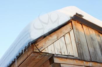 Roof of rustic wooden buildings covered with snow against the blue sky in the rays of the setting sun. View from below 