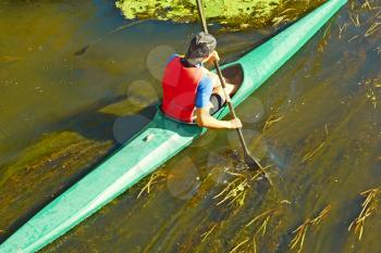 Canoeist in a canoe floating on the river overgrown with algae in a sunny day, the view from above