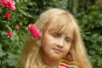 Beautiful little Caucasian girl in park near the rose bush