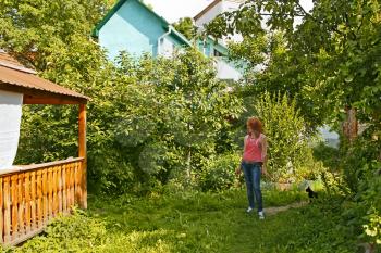 Beautiful young women on the yard among green summer trees in rural location