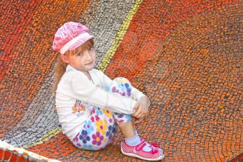 Beautiful little pretty girl sitting on the large mosaic panel with small colorful stones